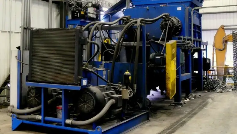Blue industrial baling machine with hydraulic hoses, cooling radiator, and electric motor on a factory floor